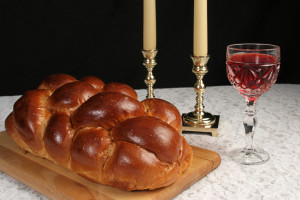 A table set for Shabbat with challah bread, candlesticks and wine. Black background, complete view.